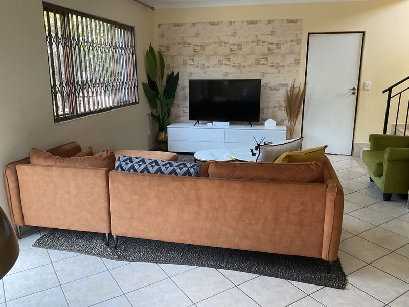 A comfortable living room featuring tiled flooring, a security gate on the window, and direct access to the staircase.