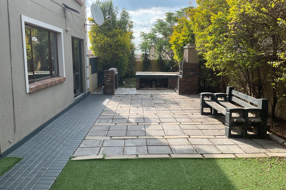 Rear exterior area featuring a paved patio, built-in braai, and artificial lawn, providing a functional outdoor entertainment space.