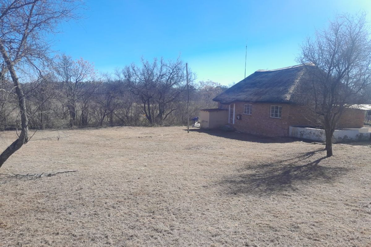 A view of the rear exterior of a farm-style dwelling featuring a traditional thatched roof and brick construction set within a large, dry garden area.