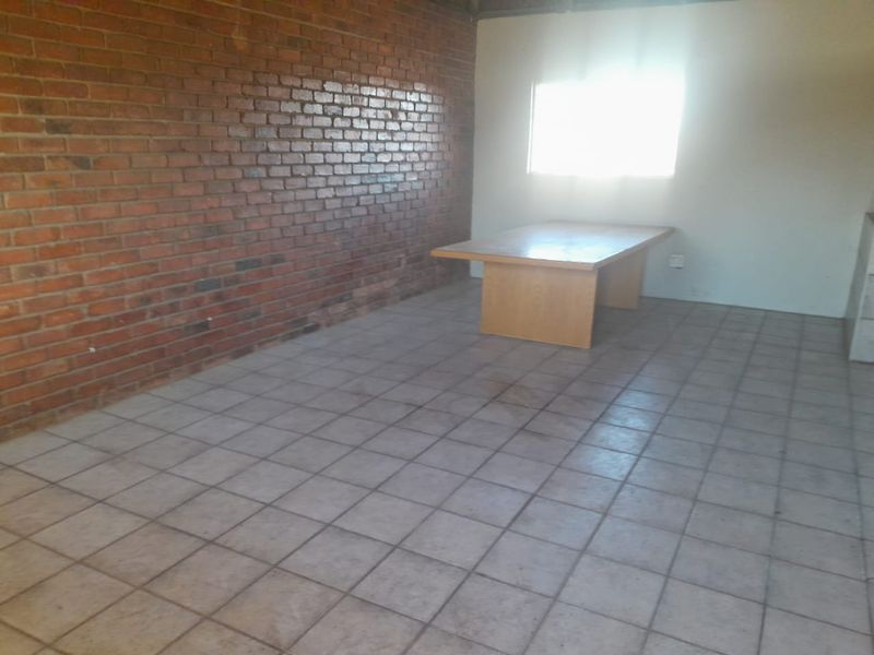 A spacious living area featuring an exposed brick feature wall and ceramic tiled flooring, offering a blank canvas for renovation.