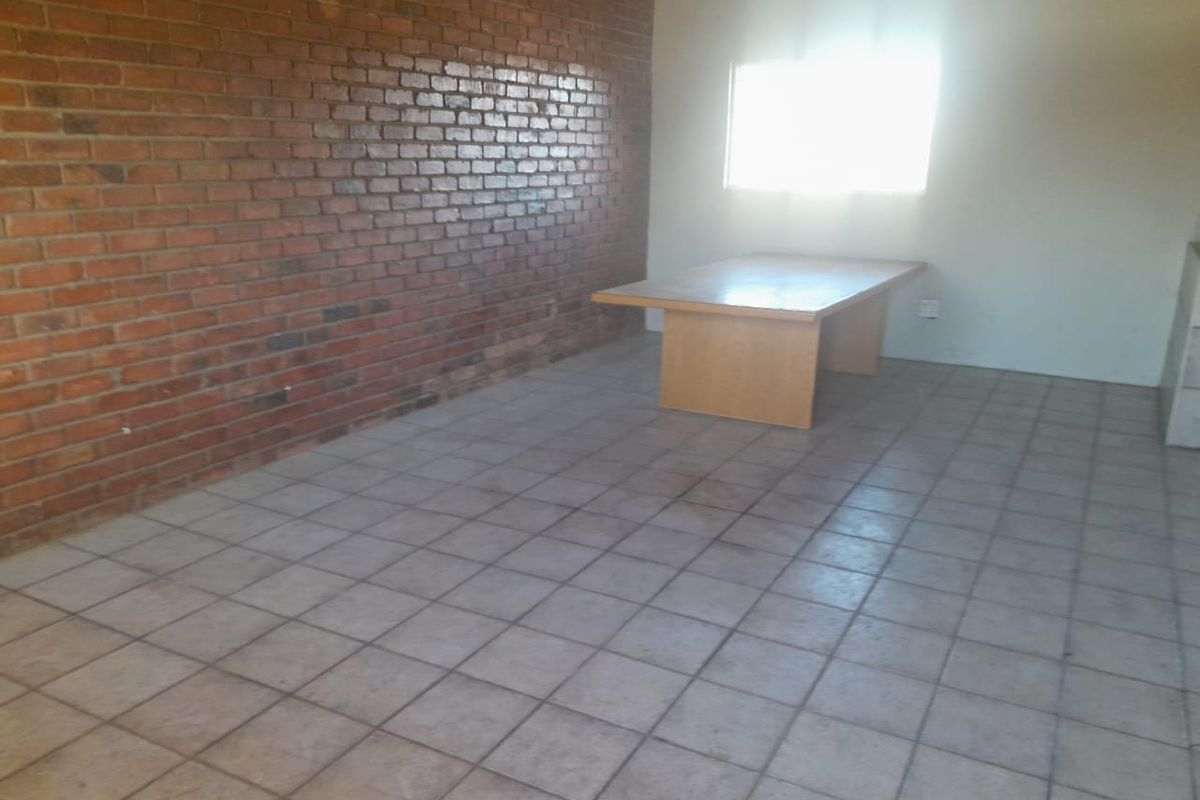 A spacious living area featuring an exposed brick feature wall and ceramic tiled flooring, offering a blank canvas for renovation.