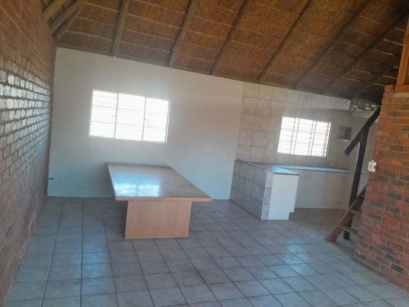 Open-plan living and kitchen area featuring a high thatched ceiling, exposed brick walls, tiled flooring, and a functional kitchen layout.