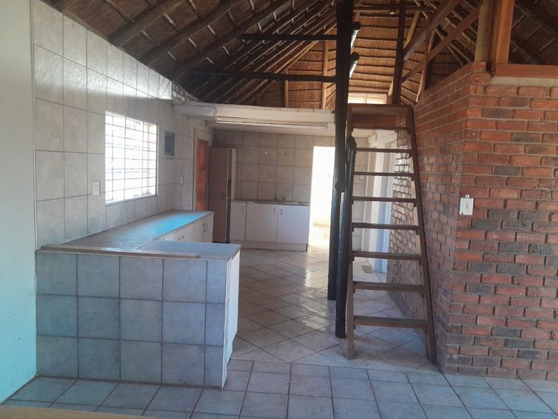 Open plan living and kitchen area featuring a rustic thatched roof, exposed brickwork, tiled surfaces, and a wooden staircase leading to an upper level.