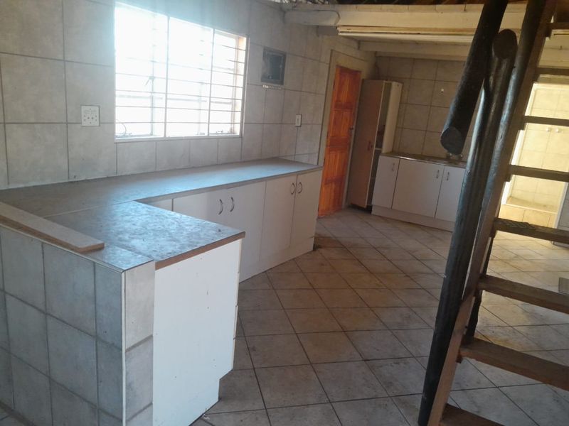 An empty kitchen area featuring tiled walls and floors, built-in cabinetry, and a wooden staircase leading to an upper level.