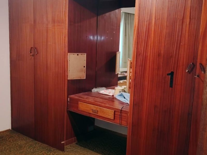 Bedroom featuring extensive built-in wooden cabinetry with an integrated vanity desk and ceiling fan, requiring cosmetic updates to modernize the space.