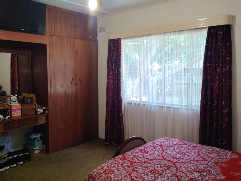 A bedroom featuring built-in wooden cabinetry with an integrated vanity and a large window, offering a functional space with potential for modernization.