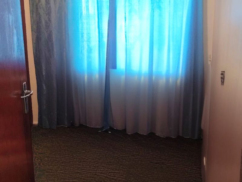 An empty bedroom featuring carpeted flooring and a window with a curtain rod, requiring cosmetic updates to the wall surfaces.