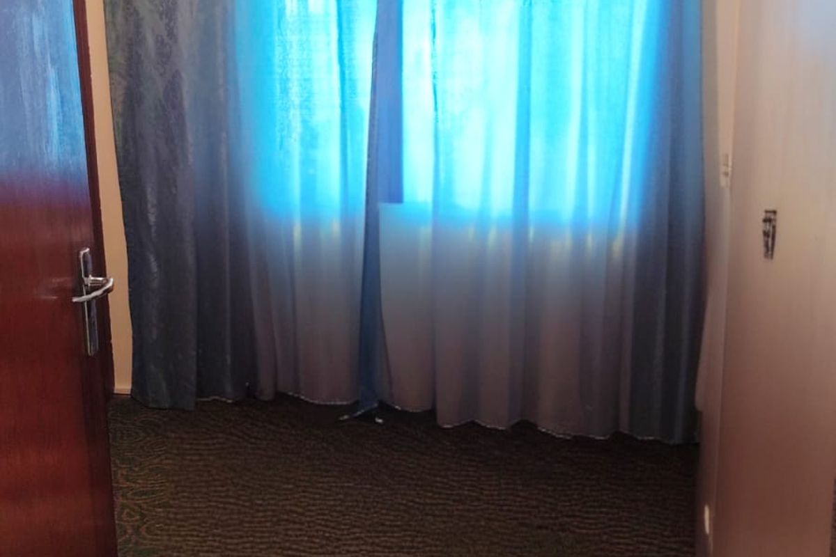 An empty bedroom featuring carpeted flooring and a window with a curtain rod, requiring cosmetic updates to the wall surfaces.