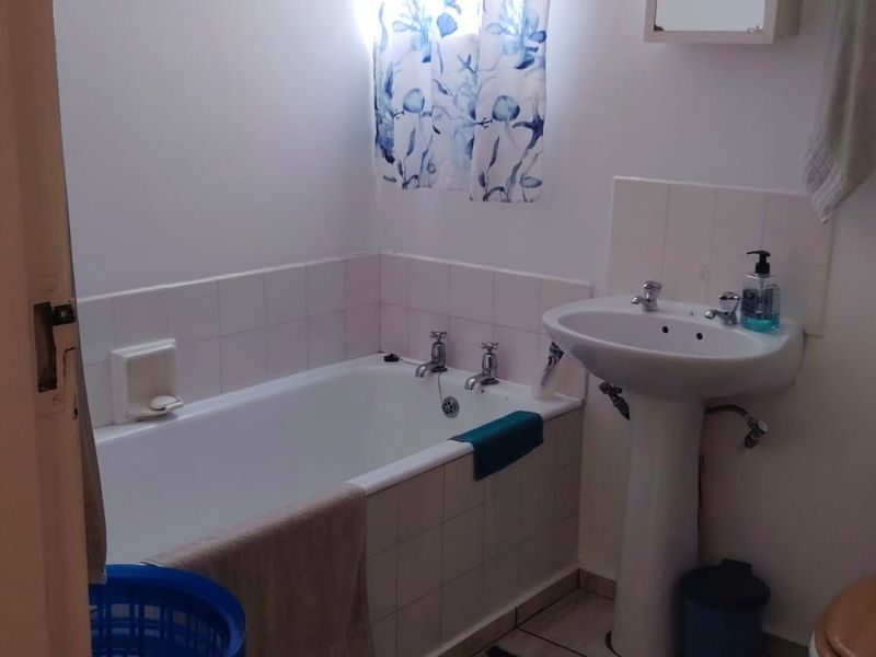 A functional bathroom featuring a pedestal basin, built-in bathtub with tiled splashback, and tiled flooring.