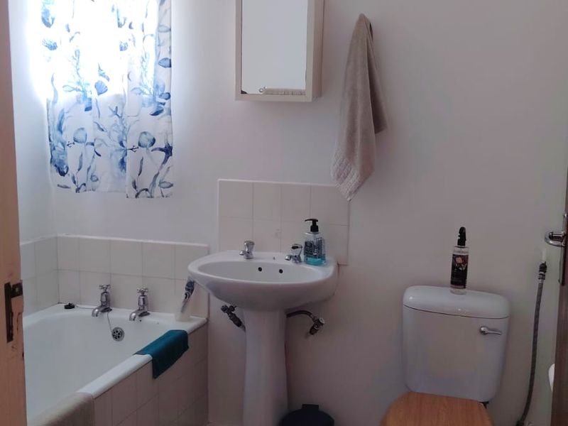 A functional bathroom featuring a bathtub, pedestal basin, and toilet with tiled flooring and neutral wall finishes.
