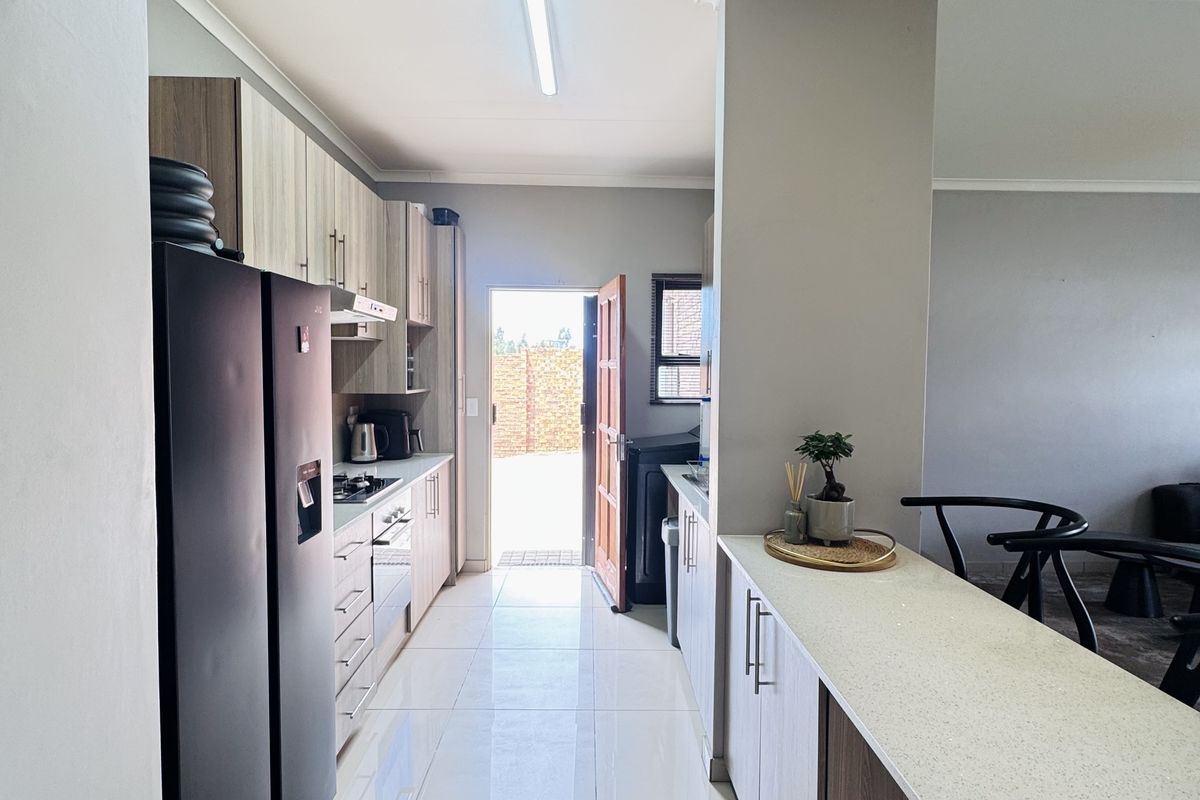 Modern kitchen featuring sleek built-in cabinetry, stone countertops, a breakfast bar, and integrated appliances, leading directly to an exterior doorway.