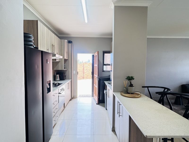 Modern kitchen featuring sleek built-in cabinetry, stone countertops, a breakfast bar, and integrated appliances, leading directly to an exterior doorway.