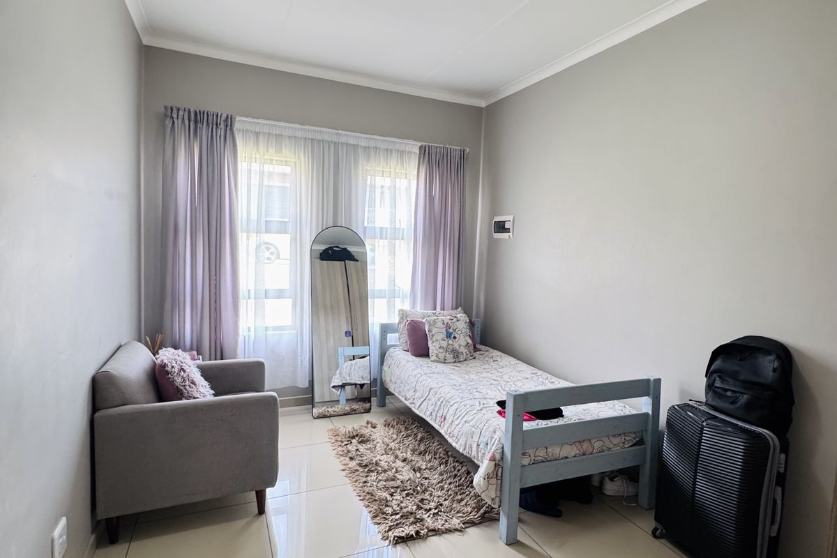 A well-lit bedroom featuring neutral wall tones, large format floor tiles, and ample natural light through the window.