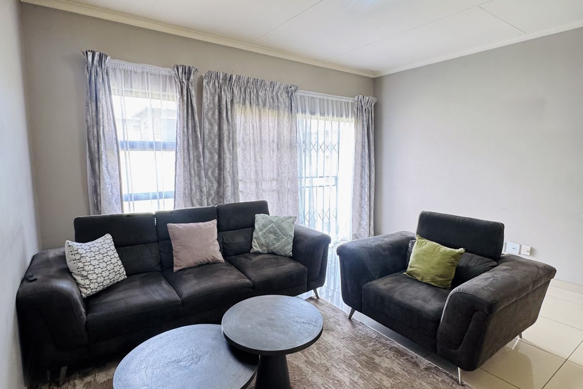 A bright and well-maintained living room featuring neutral tiled flooring and large windows with security gates, providing a comfortable and functional living space.
