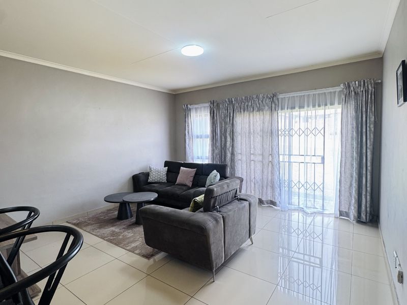 Spacious open-plan living area featuring polished tiled flooring, neutral wall tones, and a large sliding glass door with security gate providing natural light.