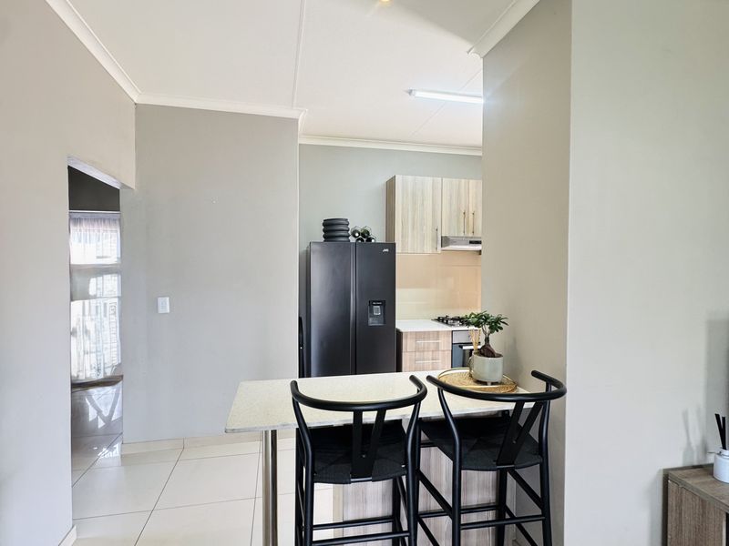 An open-plan living and kitchen area featuring modern cabinetry, built-in appliances, and neutral tiled flooring throughout.