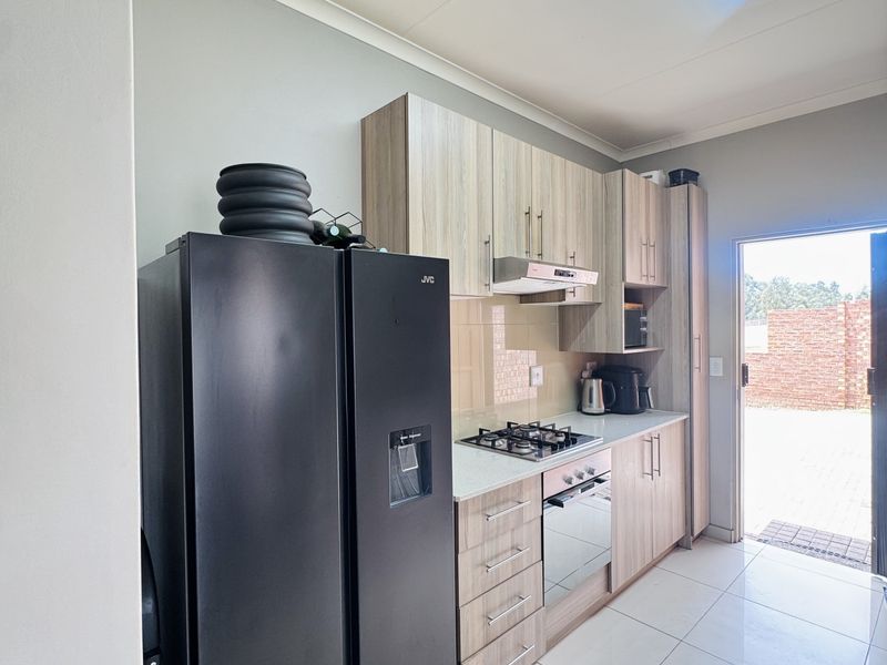 Modern kitchen featuring light wood-finish cabinetry, gas hob, built-in oven, extractor fan, and tiled flooring with direct access to the exterior.