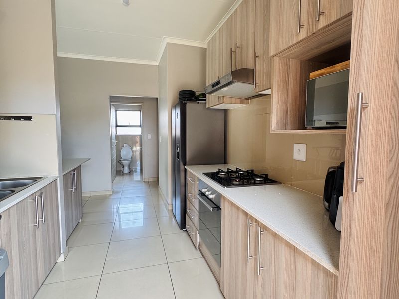 Modern kitchen featuring wood-finish cabinetry, stone countertops, built-in gas hob, oven, and extractor fan, with tiled flooring throughout.
