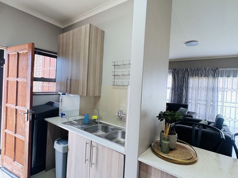 Compact scullery area featuring modern laminate cabinetry, stone countertops, and a double bowl sink, conveniently positioned adjacent to the main living space.