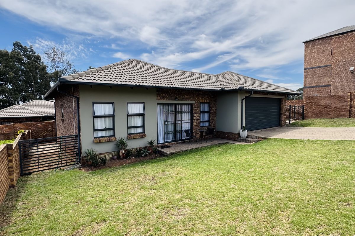 Rear view of a well-maintained townhouse featuring a tiled roof, brick exterior, double garage, and a spacious private lawn area.