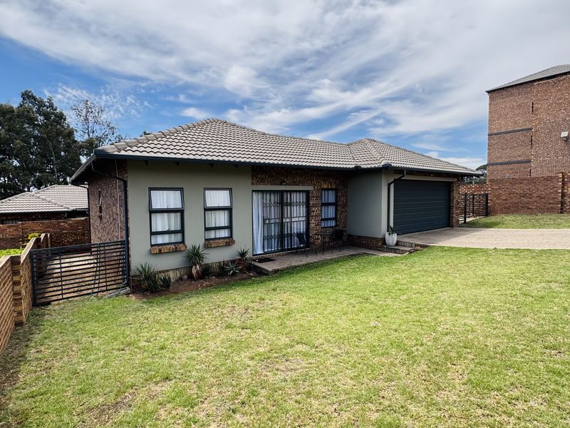 Rear view of a well-maintained townhouse featuring a tiled roof, brick exterior, double garage, and a spacious private lawn area.