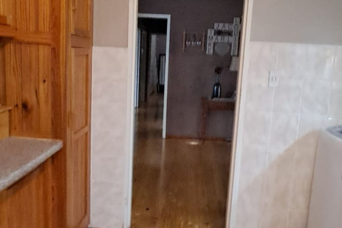 A functional kitchen area featuring tiled flooring, a tiled splashback, and built-in wooden cabinetry, with a doorway leading into the adjacent living space.