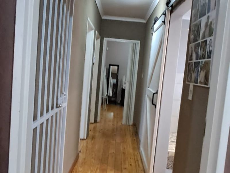 A functional hallway featuring polished timber flooring, a sliding barn door, and a security gate, providing access to multiple rooms.