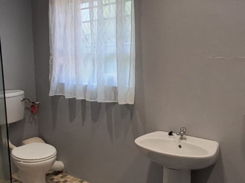 A functional bathroom featuring a pedestal basin, toilet, and a glass-enclosed shower area with tiled flooring.