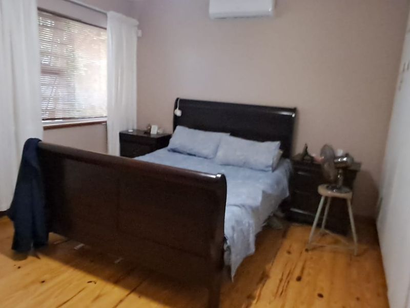 A bedroom featuring timber flooring, built-in cupboards, and a wall-mounted split-system air conditioner.