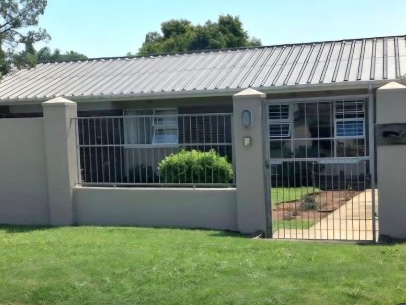 Front view of the property featuring a metal roof, secure perimeter wall with metal fencing, and a gated entrance with a paved walkway.