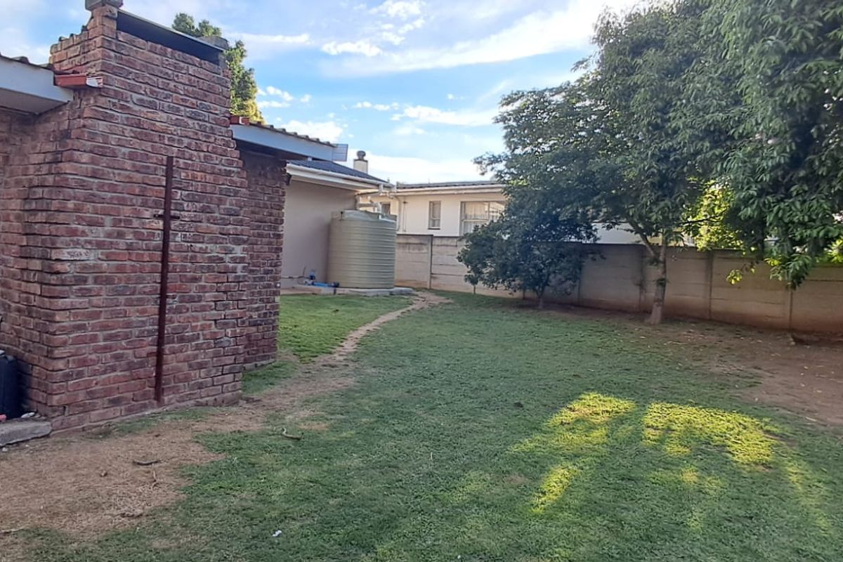 A rear garden area featuring a brick chimney structure, a water tank, and a precast concrete boundary wall.