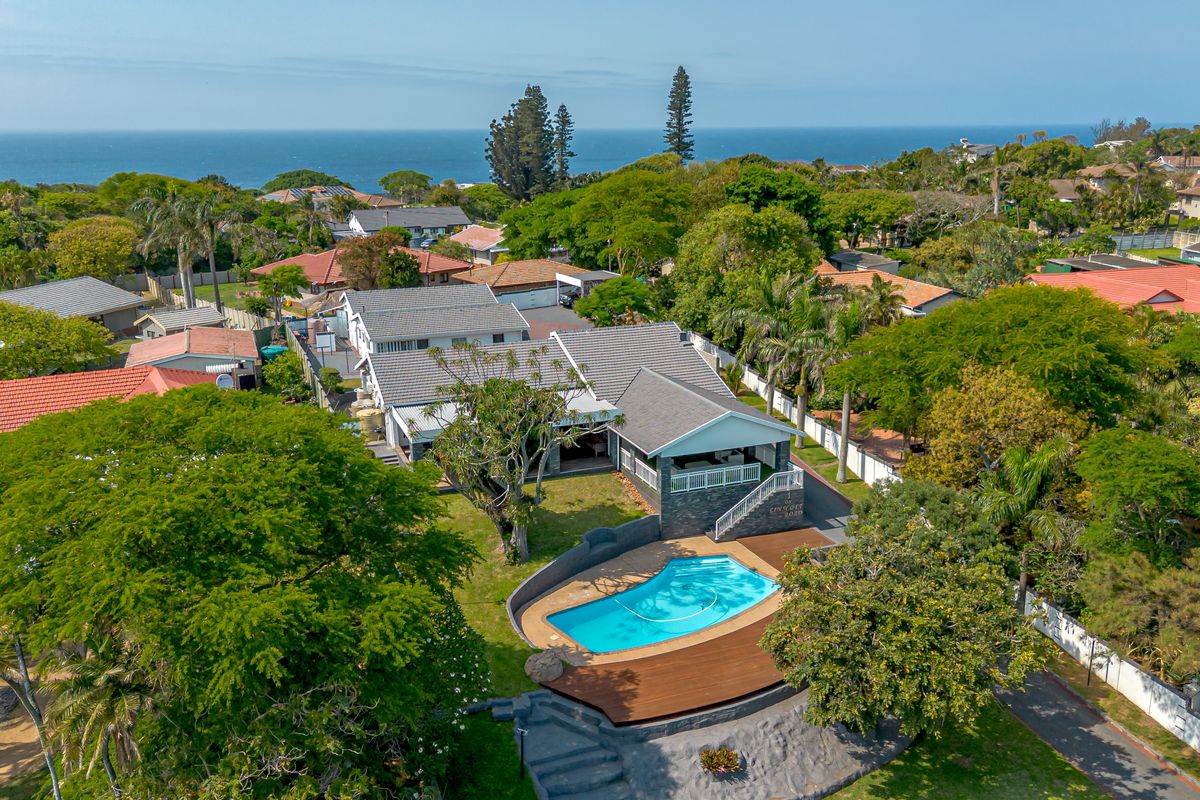 Aerial view of a residential property featuring a swimming pool, wooden decking, and a spacious garden with ocean views in the background.