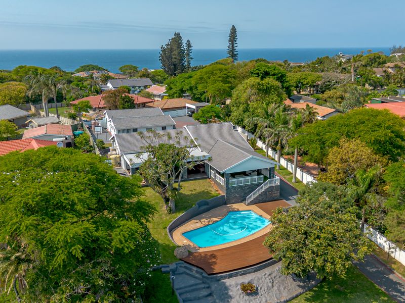Aerial view of a residential property featuring a swimming pool, wooden decking, and a spacious garden with ocean views in the background.