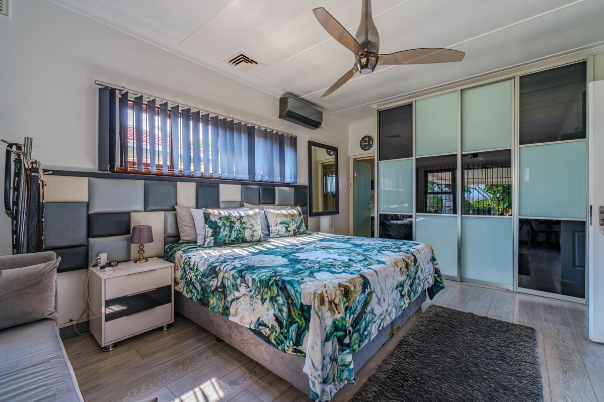 A well-maintained bedroom featuring built-in sliding door wardrobes, a ceiling fan, split system air conditioning, and modern laminate flooring.