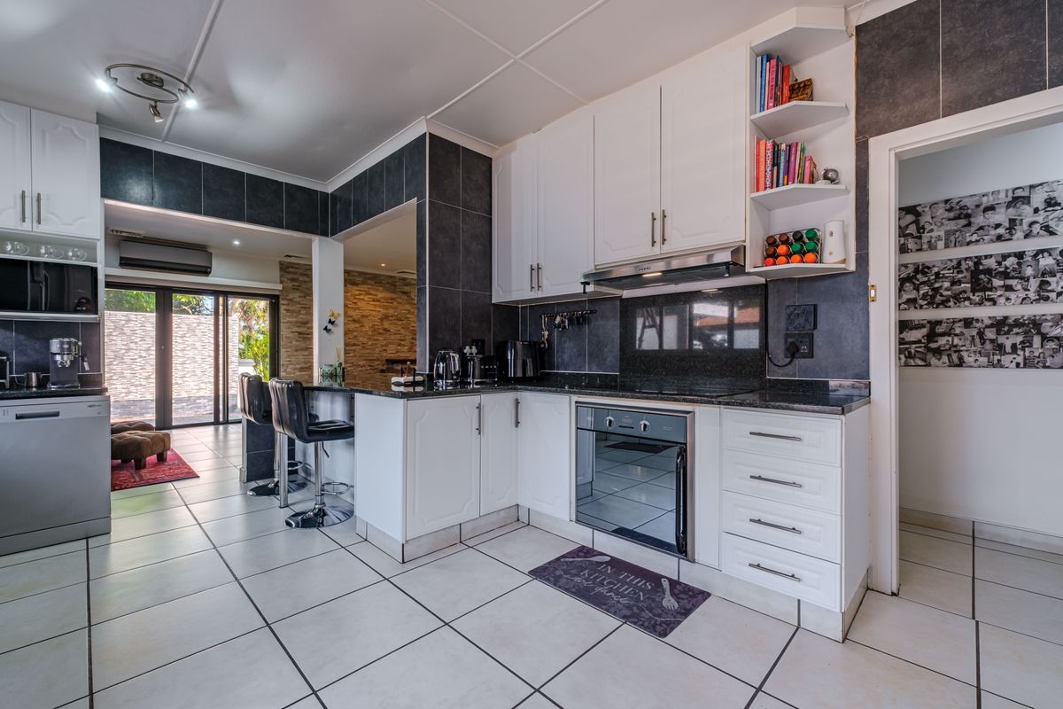 Modern open-plan kitchen featuring white cabinetry, granite countertops, built-in oven, extractor fan, and tiled flooring, seamlessly connecting to the adjacent living area.