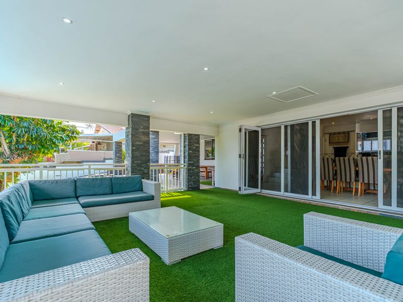 Spacious covered patio featuring stone-clad pillars, artificial grass flooring, and large sliding glass doors providing seamless access to the interior living area.