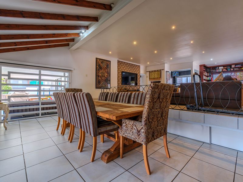 Spacious open-plan living and dining area featuring exposed timber ceiling beams, tiled flooring, and a raised platform section with built-in shelving.