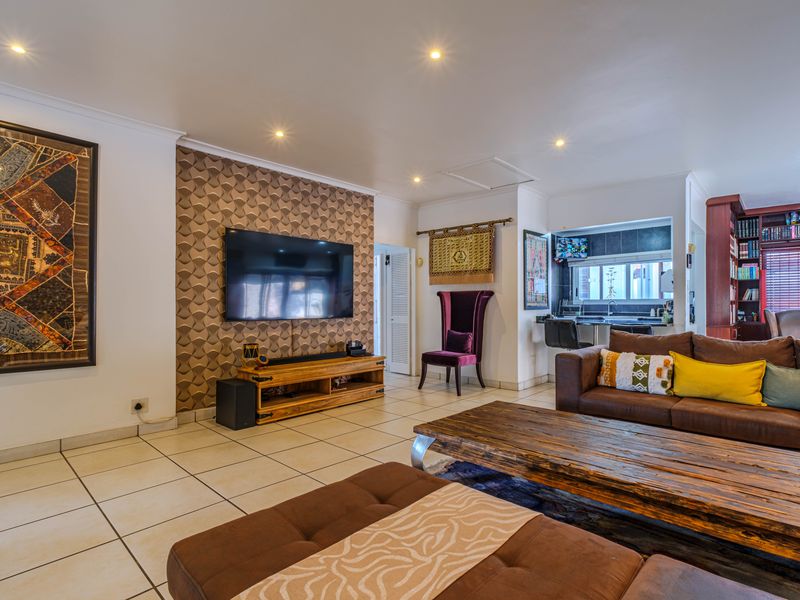 Spacious open-plan living area featuring tiled flooring, recessed lighting, and a seamless transition to a functional kitchen space with built-in cabinetry.