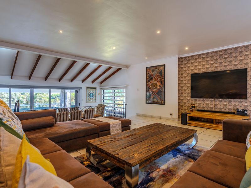 Spacious open-plan living area featuring exposed timber ceiling beams, tiled flooring, and large sliding glass doors leading to an outdoor space.