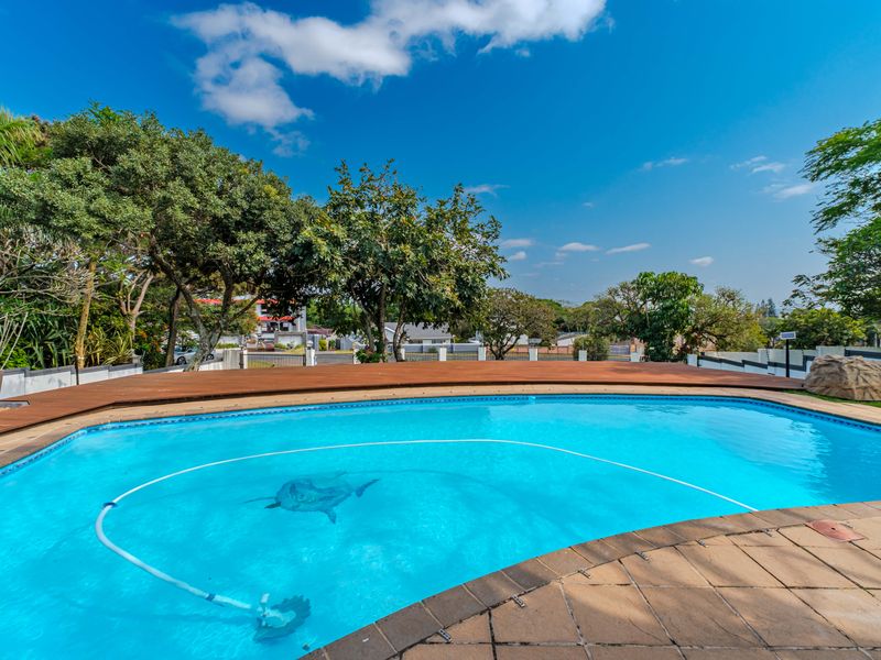 A well-maintained swimming pool area featuring a wooden deck, tiled surround, and established garden surroundings.