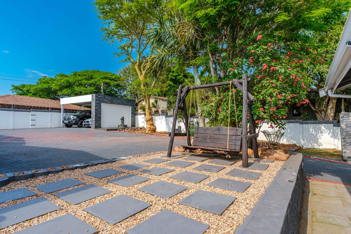 A well-maintained rear exterior area featuring a paved driveway, a modern carport, and landscaped garden space with stone pathways.