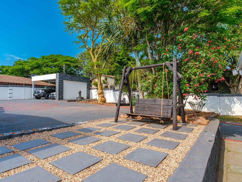 A well-maintained rear exterior area featuring a paved driveway, a modern carport, and landscaped garden space with stone pathways.