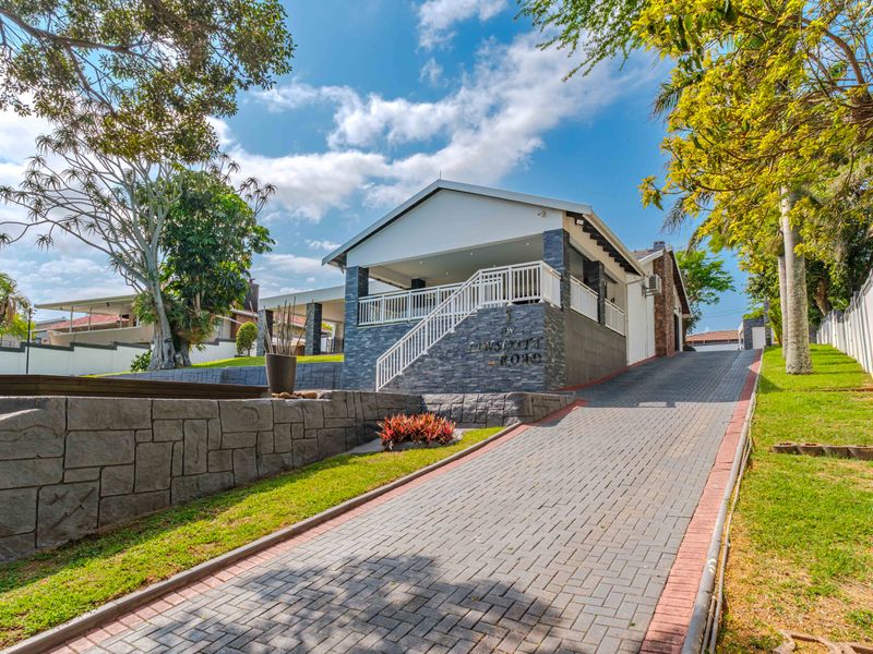 Front elevation of a well-maintained house featuring a paved driveway, stone-clad facade, and an elevated covered patio entrance.