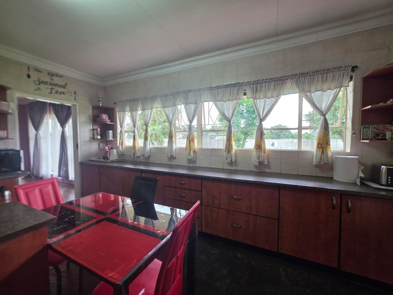 A functional kitchen featuring extensive built-in cabinetry, laminate countertops, and a tiled backsplash, with large windows providing natural light and garden views.