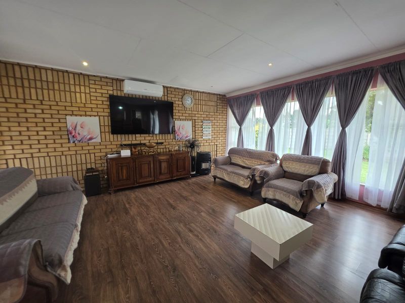 Spacious living room featuring exposed brick walls, laminate flooring, and large windows with curtains, providing a comfortable and well-lit area.