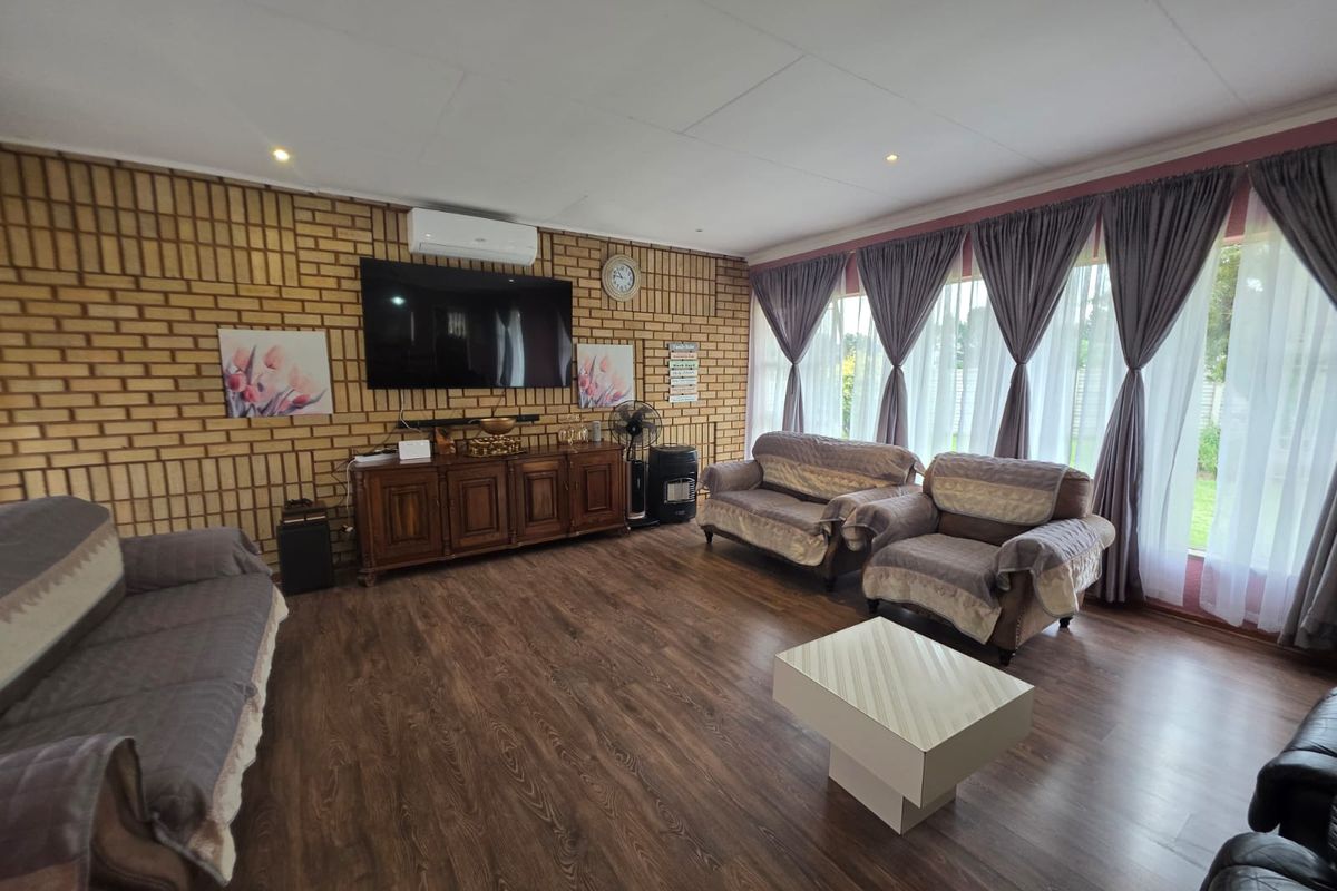 Spacious living room featuring exposed brick walls, laminate flooring, and large windows with curtains, providing a comfortable and well-lit area.