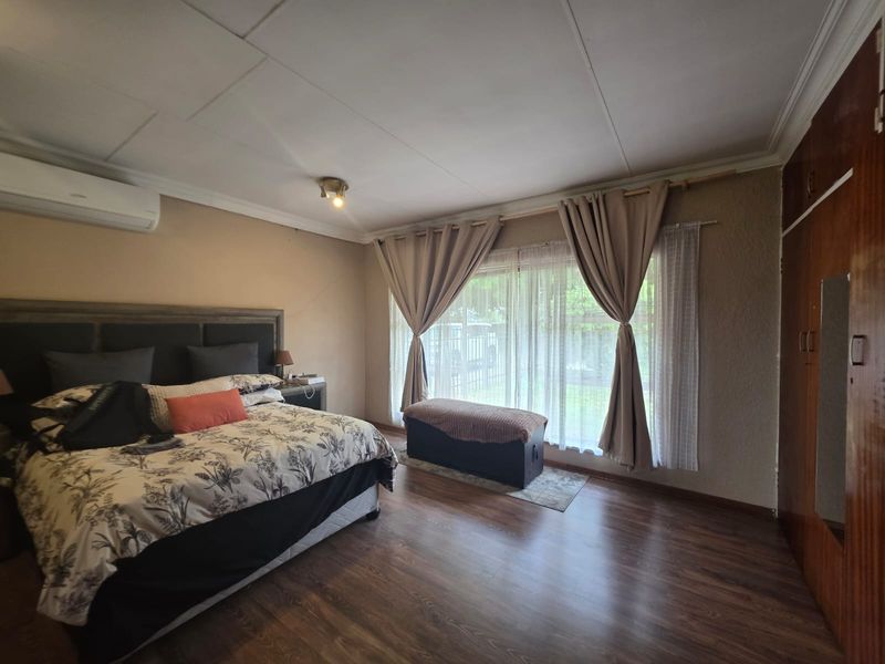 Spacious bedroom featuring laminate flooring, built-in cupboards, and an air conditioning unit, with large windows providing natural light.