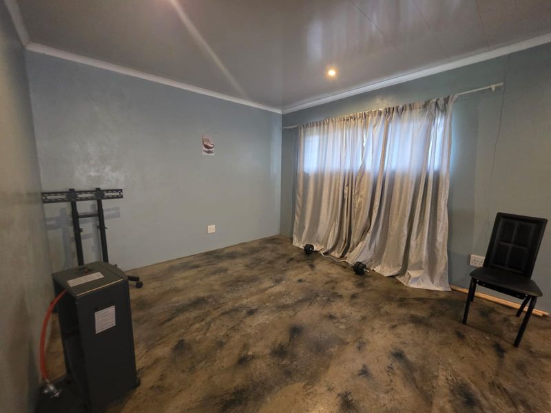 A sparsely furnished bedroom featuring a concrete floor finish, light blue walls, and a curtained window.