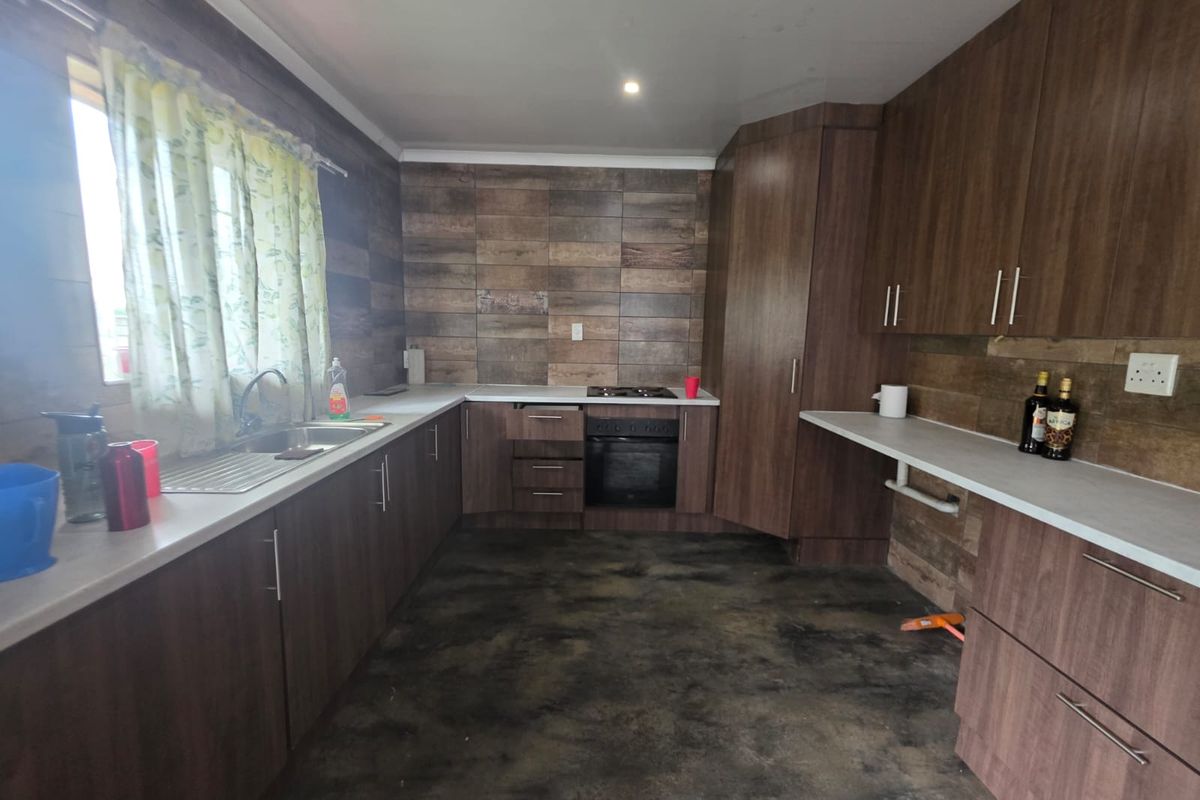 A functional kitchen featuring wood-look cabinetry, laminate countertops, a built-in oven with gas hob, and a tiled splashback.