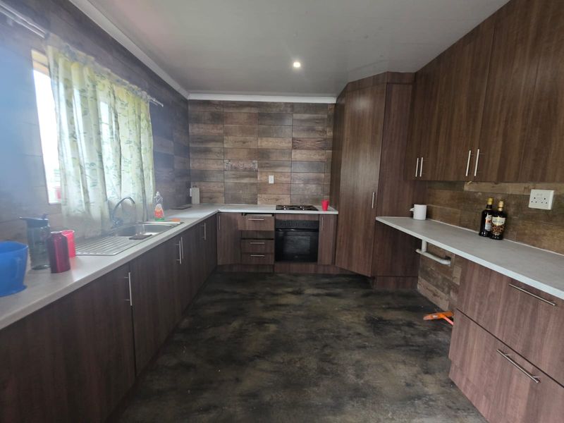 A functional kitchen featuring wood-look cabinetry, laminate countertops, a built-in oven with gas hob, and a tiled splashback.